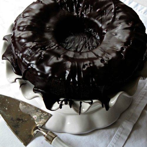 Top view of round tube pan brick street chocolate cake with chocolate drizzle frosting on a cake stand
