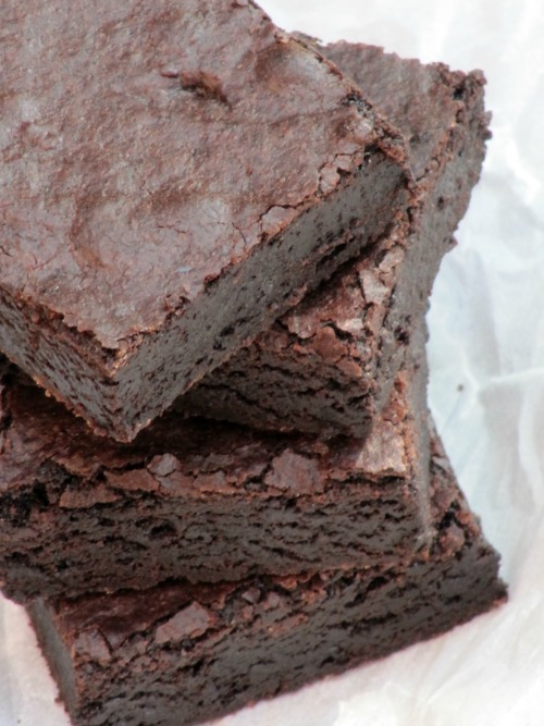 closeup image of a stack of three moist rich fudgy cocoa brownies made with cocoa powder sitting on a piece of white parchment paper.