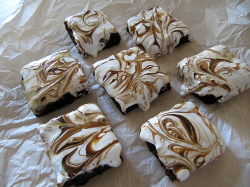 dulce de leche fluff brownies sitting on a piece of parchment paper are covered with a thick layer of fluffy marshmallow topping with swirls of caramerl sauce.