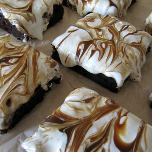 overhead shot of chocolate brownies topped with marshmallow fluff and swirls of dulce de leche are sitting on parchment paper