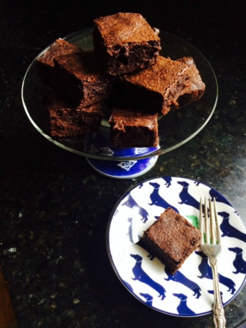 Overhead view of a vlue and white footed cake stand holding several large square classic fudge brownies with a single brownie on a blue and white plate in front.