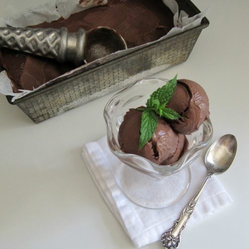 loaf pan with homemade dark chocolate ice cream next to a glass bowl with two scoops of chocolate ice cream.