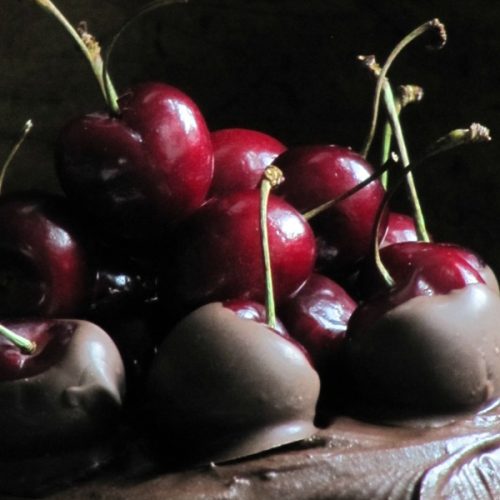 close-up photo of chocolate cherry filled cake top with chocolate dipped cherries and whole fresh cherries on top.