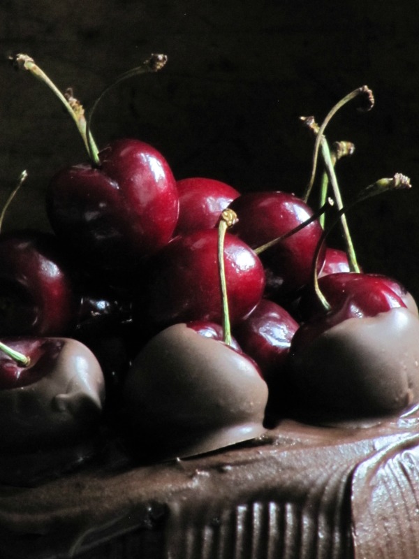 Close-up photo of chocolate cherry filled cake top with chocolate dipped cherries and whole fresh cherries on top.