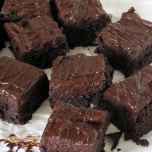 Large thriple chocolate frosted fudge brownies with chocolate ganache topping on a piece of white parchment paper