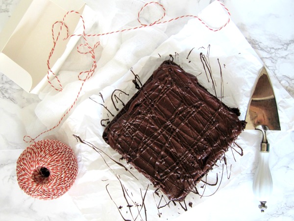 Overhead view of a rich ganache-glazed triple chocolate frosted fudge brownie with bittersweet chocolate chips inside sitting on a piece of white parchment paper.