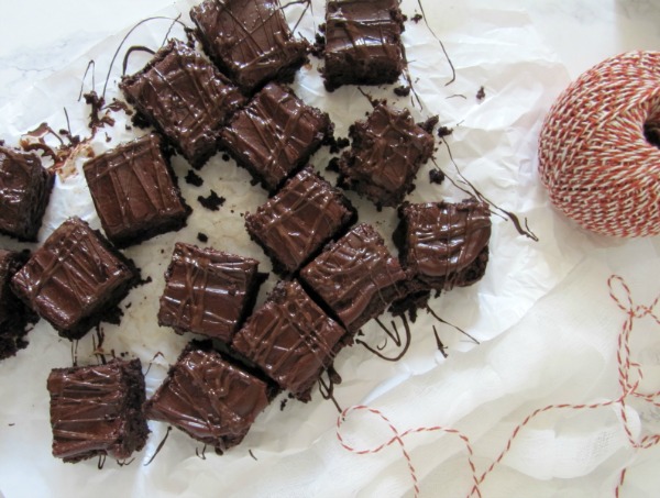 Overhead shot of a large pile of triple chocolate frosted fudge brownies with chocolate chips inside and ganache frosting sitting on a piece of white crumpled parchment paper.