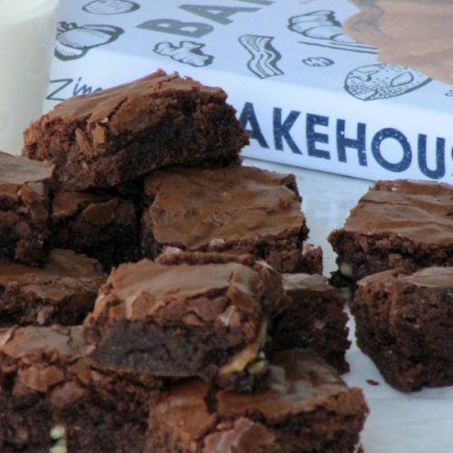 Large pile of Zingerman's Bakehouse Black Magic Brownies and piece of white parchment paper in front of the bakehouse cookbook.