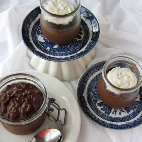 overhead view of a table with small jars holding bailey's irish cream chocolate rice pudding topped with whipped cream and served with a spoon.
