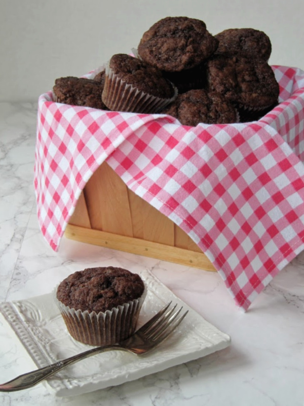 white plate with a double chocolate muffin next to a basket of muffins.