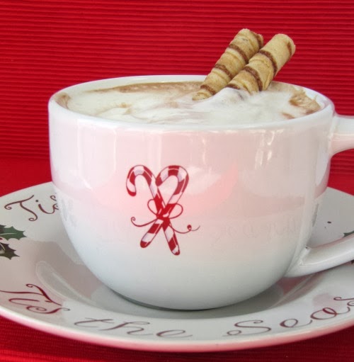 closeup side view of a white Christmas mug filled with hershey's perfectly chocolate hot cocoa topped with whipped cream and garnished with two Pirouline rolled wafer cookies. The mug is on a Christmas plate against a red background