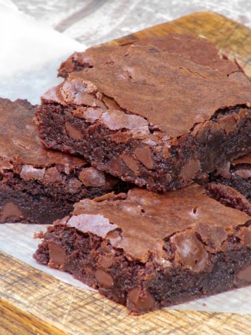 Three baked chocolate fudge brownies sit on a piece of white parchment paper on a wood surface