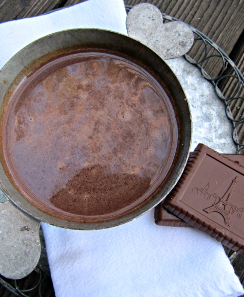 closeup view from overhead of a large mug of French chocolat chaud from  Dorie Grenspan sitting on a white napkin next to two pieces of block chocolate on a silver tray.