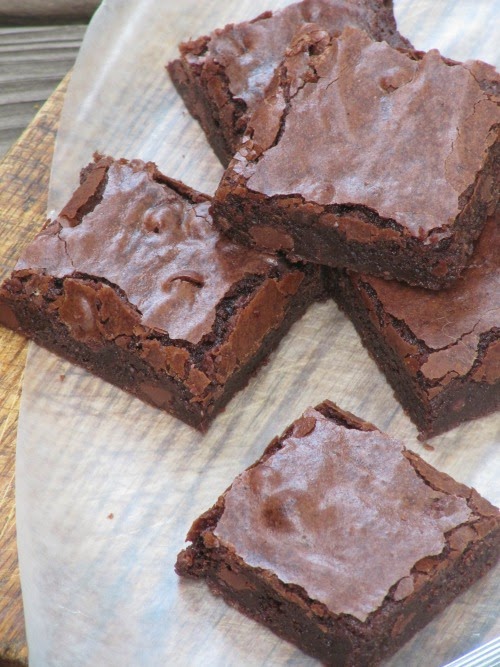 Close up view of baked chocolate fudge filled with chocolate chips sitting on a piece of white parchment on a wood cutting board.