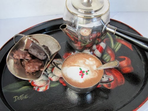 overhead view of a cup of rich dark Wittamer hot chocolate on a colorful tray next to a serving dish of chocolate candies and a silver hot chocolate pot.