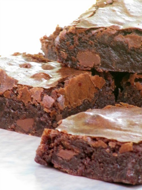 up close view of three dark baked chocolate fudge with crispy tops against a white background.