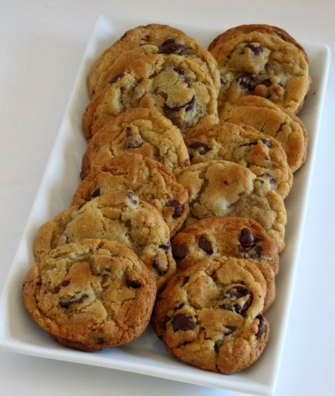 a white retangular tray filled with two rows of large dark chocolate chip cookies by jacques torres sits on a wihite surface