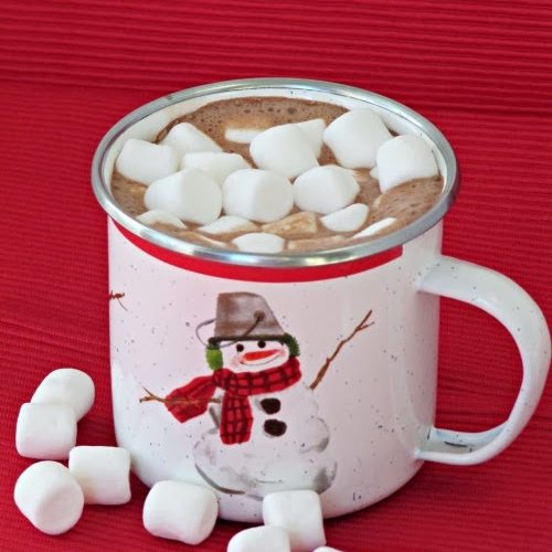 Closeup view of mocha hot chocolate with marshmallows in a white cup with a snowman on it and several mini-marshmallows scattered on a red surface.