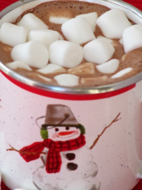 Close up photo of a white mug with a snowman decoration filled to the top with rich mocha hot chocolate with marshmallows floating on top.