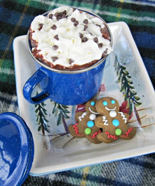 Overhead view of a large bright blue mug of polar express hot chocolate made with dark chocolate and sweetened condensed milk topped with whipped cream and chocolate bits. THe mug is ona white seasonally decorated tray along with gingerbread cookies.