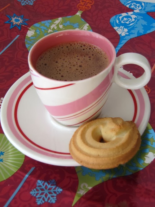 Pink and white peppermint design cup and saucer with the cup holding Bicerin italian chocolate coffee drink along with a vanilla sugar cookie of the saucer. The cup and saucer is on a colorful bqackground