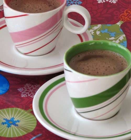 Two peppermint striped cups and saucers, one pink and white, one green and white, both filled with Bicerin coffee and chocolate drink. The cups are on a colorful table cloth.
