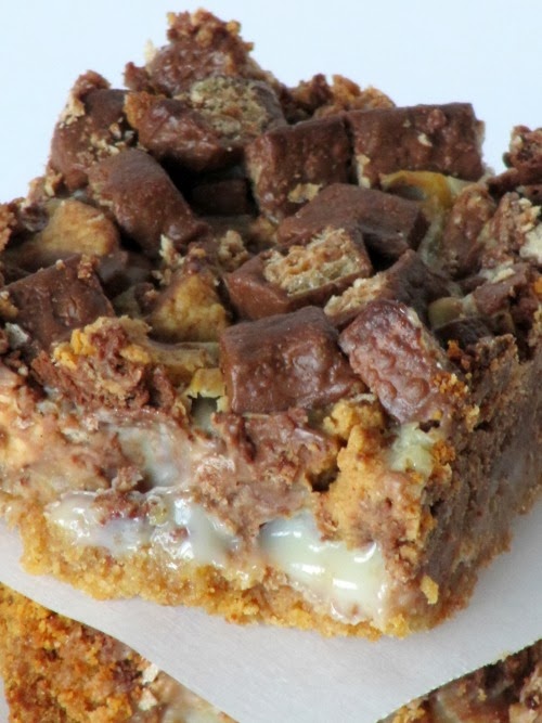Closeup view of a large chocolate peanut butter chunk magic bars square showing the graham cracker crust, a layer of sweetened condensed milk, and topped with melted kit-kat and peanut butter cup chunks.