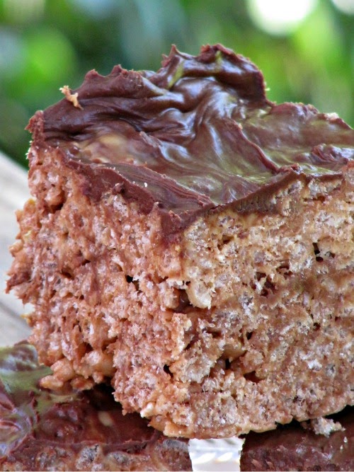 Reese's Peanut Butter Rice Krispies treats with dark chocolate topping are stacked in front of a green bakground.