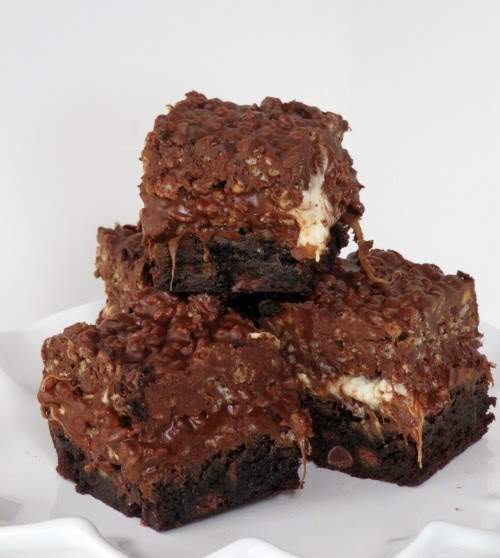 A cluster of dark brown rolo  marshmallow peanut butter  brownies made with peanut butter and rice krispies sits on a white surface against a white background.