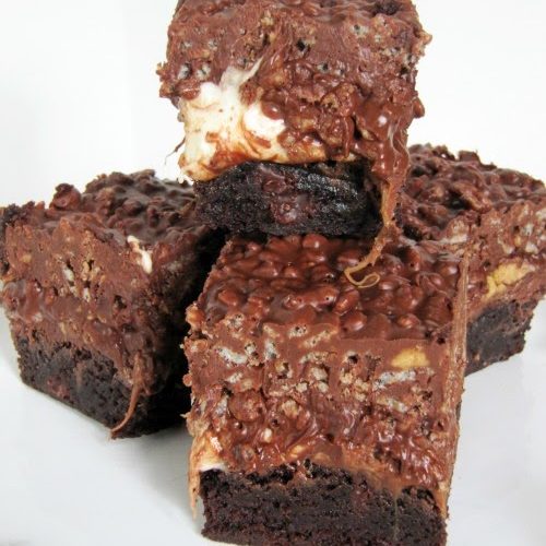 Four dark chocolate brownies made with peanut butter, marshmallows rolo candies and rice krispies sit in a cluster on a white surface against a white background.