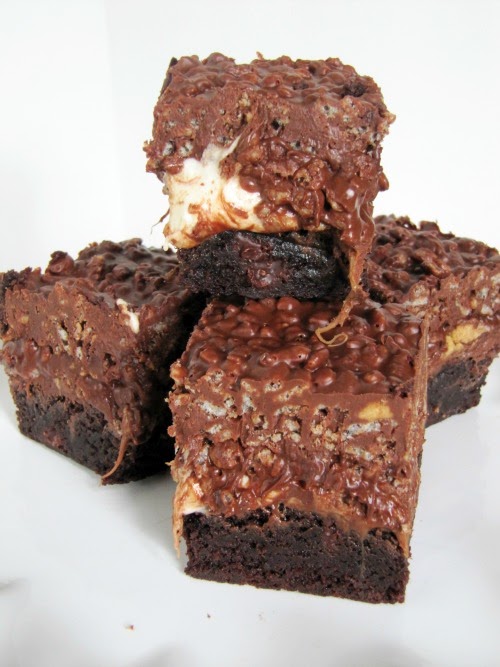 Four dark chocolate brownies made with peanut butter, marshmallows rolo candies and rice krispies sit in a cluster on a white surface against a white background.