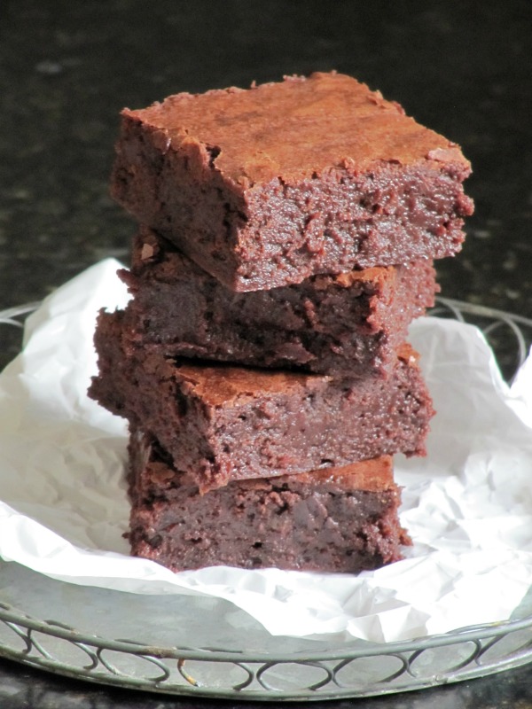 A cloeup of a stack of four fudgy Baked Bakery NY aka Oprah's favorite brownies are sitting on a piece of white parchment against a dark background.