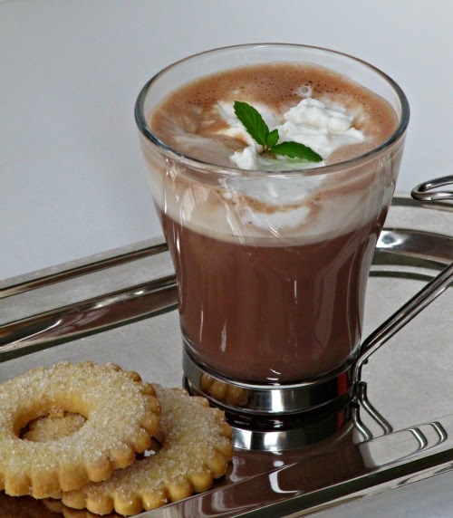 close view of a tall glass of basil mint hot chocolate drink on a silver tray with two vanilla sugar cookies.