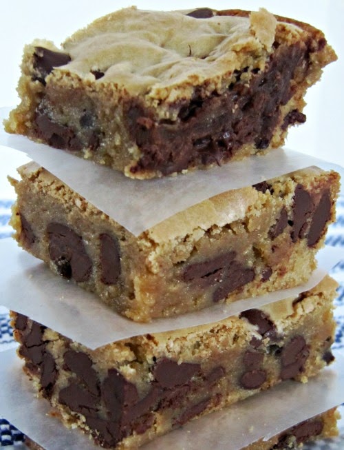 A closeup image of three triple chocolate blondies with chocolate chip filling, each blondie brownie separated by a piece of white parchment paper.