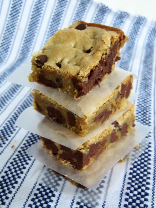 An angled overhead view of a stack of triple chocolate blondie bar cookies with crispy tops and chocolate chip-filled centers on a navy and white striped woven table cloth.