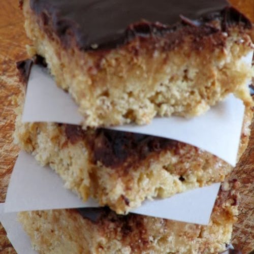 Closeup view of a stack of peanut butter browned butter rice krispies treats with chocolate ganache topping seaprated with pieces of white parchment paper.