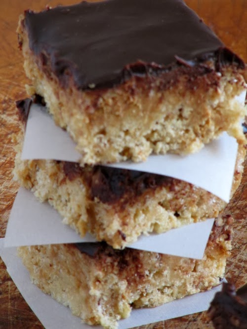 Closeup view of a stack of browned butter peanut butter cup rice krispies treats with chocolate ganache topping separated with pieces of white parchment paper.