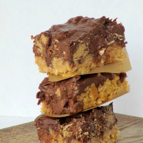 A stack of three luscious peanut butter pretzel bars with melted chocolate chip and pretzel topping and made with rice krispie cereal is sitting on a wood surface.