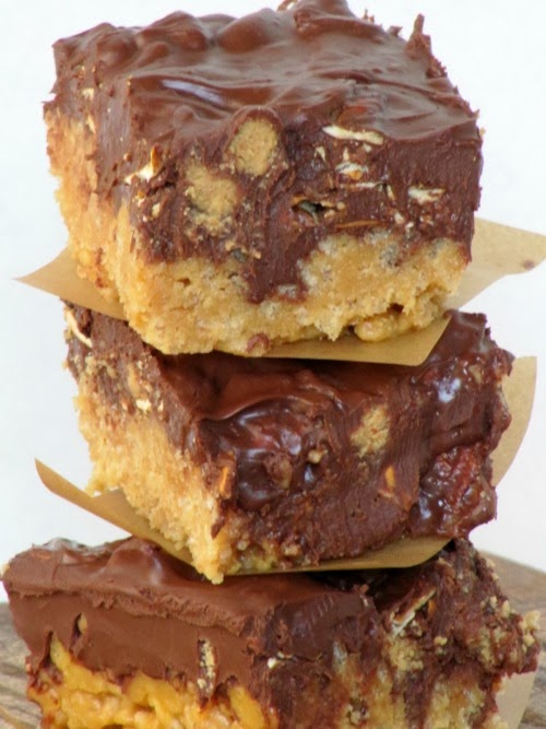 A closeup of a stack of peanut butter pretzel bars made with rice krispies, pretzels, chocolate chips and Reese's peanut butter pumpkins have parchment separating the bars.