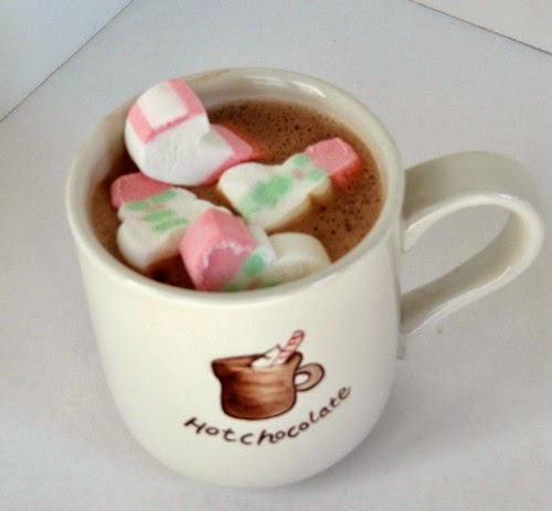 overhead view of a white mug on a white background. The mug says "hot Chocolate" with a mug of chocolate on it and is filled with raspberry hot chocolate made with raspberry Chambord liqueur and topped with colorful christmas marshmallows.