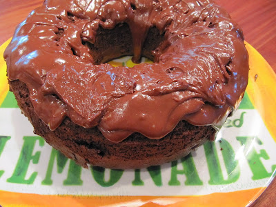 Round bundt-style choco-holic cake with chocolate frosting on a yellow, white and green placemat that says "lemonade" on it.