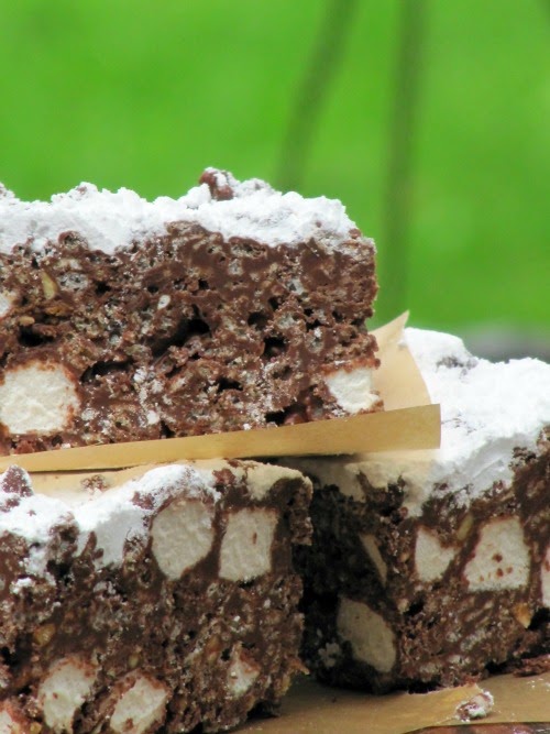 A side view of a stack of three puppy chow krispie treats made with chocolate chips, marshmallows, peanut butter and rice krispies with powdered sugar on top sitting against a green background.