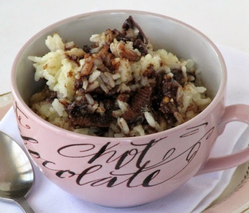 Closeup of a pink cup holding a serving of chocolate almond toffee rice pudding made with cream, sugar, rice, and a chocolate toffee candy bar, sitting on a white napkin.