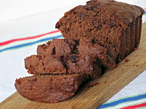 Front angled view of a rich moist half-sliced loaf of chocolate chocolate chip banana bread that contains cocoa powder, ripe bananas, warm spices and melted chocolate chips.