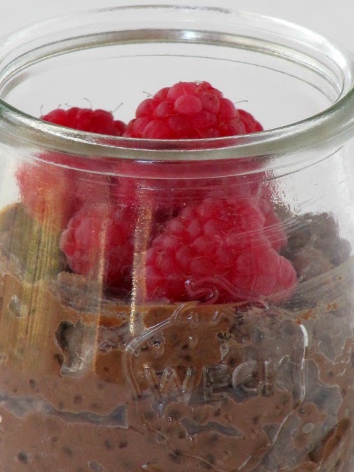 Closeup of a glass jar of chocolate tapioca pudding made with 60% dark chocolate and vanilla bean paste with fresh red raspberries on top against a white background.