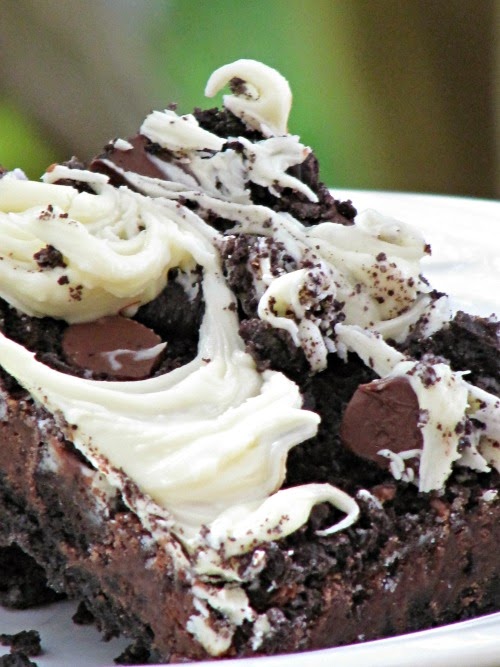 Closeup of triple chocolate Oreo bars with milk and dark chocolate centers and white chocolate swirls on top on a white plate against a green background.