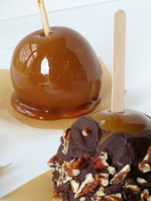A caramel apple apple and a chocolate caramel apple rolled in pistachios and dried cranberries are shown against a white background.