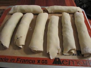 An overhead view of several tubular rolls of chocolate cranberry rugelach cookies sitting on a tray in preparation of being cut and baked.