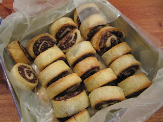 An overhead view of a large box filled with rows of lightly browned chocolate cranberry rugelach cookies filled with chocolate, nuts and cranberries along with apricot jam.