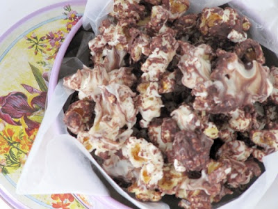 An overhead view of a white container filled with triple chocolate kettle corn covered in three kinds of melted chocolate chips.
